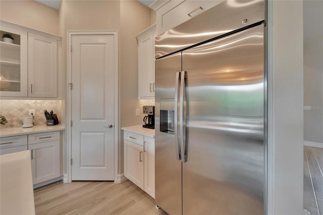 kitchen with white cabinets, stainless steel fridge, light hardwood / wood-style floors, and decorative backsplash