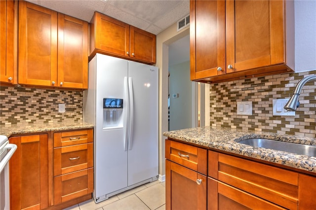 kitchen with decorative backsplash, light stone counters, sink, light tile patterned floors, and white fridge with ice dispenser