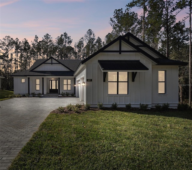 view of front of property featuring board and batten siding, decorative driveway, a yard, and a garage