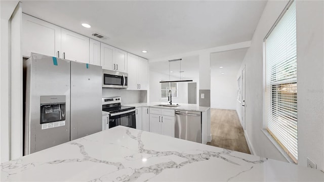 kitchen with appliances with stainless steel finishes, light hardwood / wood-style floors, white cabinetry, light stone countertops, and sink