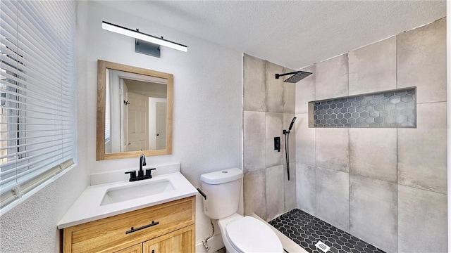 bathroom featuring vanity, toilet, a textured ceiling, and tiled shower