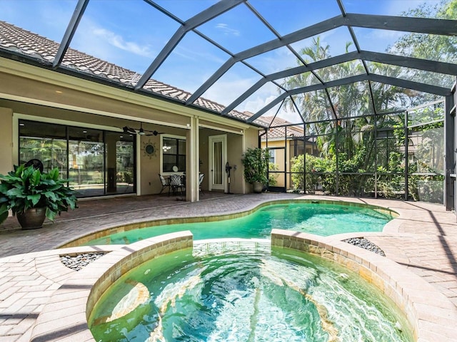 view of pool with glass enclosure, ceiling fan, a patio, and an in ground hot tub