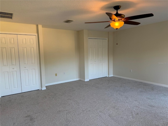 unfurnished bedroom with carpet flooring, multiple closets, ceiling fan, and a textured ceiling