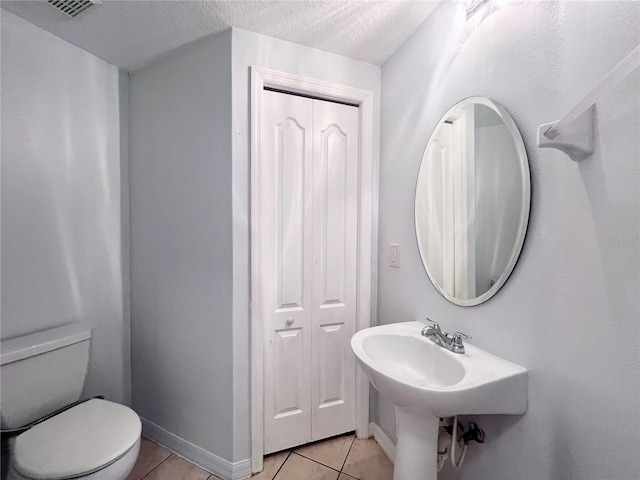 bathroom with a textured ceiling, toilet, and tile patterned floors