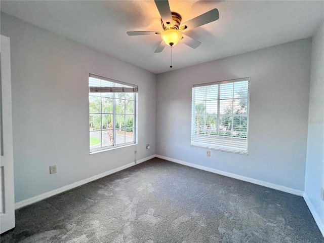 spare room featuring dark carpet, a wealth of natural light, and ceiling fan