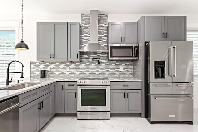 kitchen with light stone countertops, gray cabinets, stainless steel appliances, sink, and wall chimney range hood