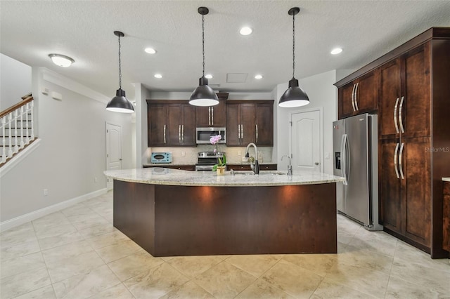 kitchen with stainless steel appliances, light stone counters, dark brown cabinetry, and a kitchen island with sink