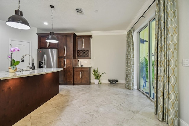 kitchen featuring light stone counters, sink, decorative light fixtures, ornamental molding, and stainless steel fridge