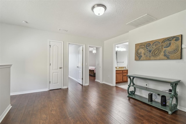 interior space with a textured ceiling, ensuite bath, and dark hardwood / wood-style flooring