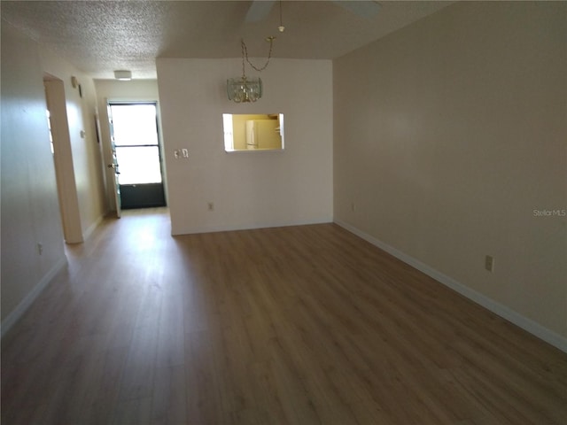 unfurnished room featuring a textured ceiling, an inviting chandelier, and dark wood-type flooring