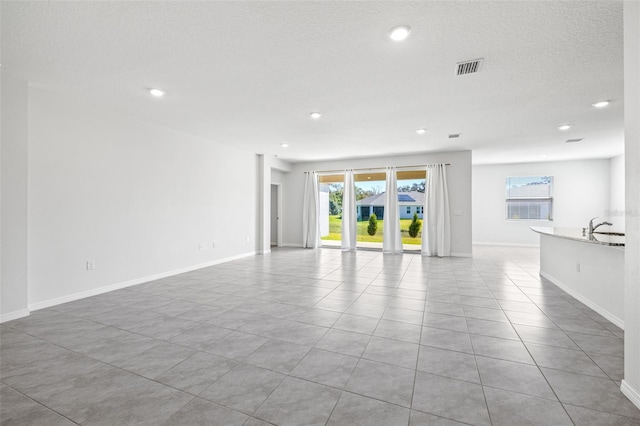 unfurnished living room with a textured ceiling, light tile patterned flooring, and sink