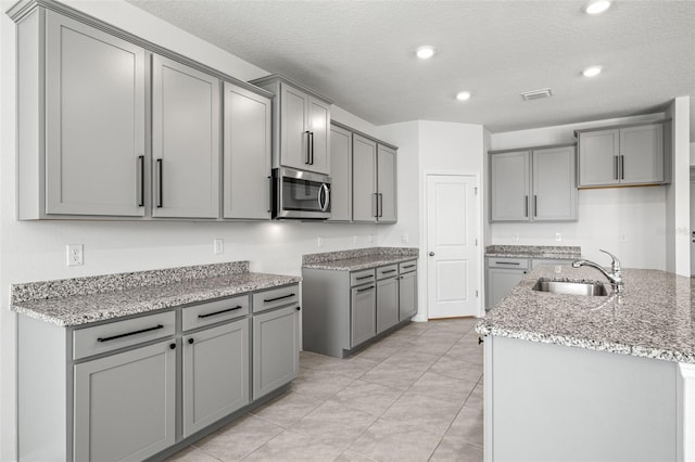 kitchen with a textured ceiling, an island with sink, sink, and gray cabinets