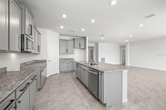 kitchen featuring gray cabinetry, stainless steel appliances, a textured ceiling, a kitchen island with sink, and sink