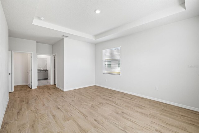 interior space with a textured ceiling, light hardwood / wood-style flooring, and a tray ceiling