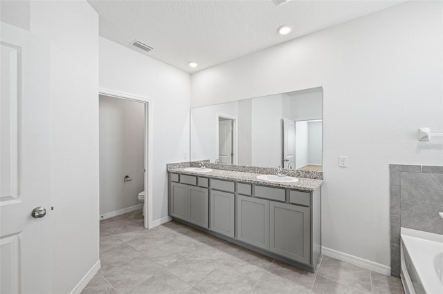 bathroom with tile patterned flooring, a textured ceiling, a tub, vanity, and toilet