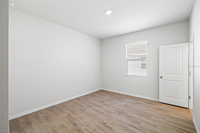 empty room with a textured ceiling and light hardwood / wood-style flooring