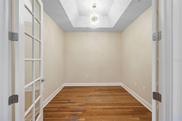 spare room with hardwood / wood-style floors, a notable chandelier, and a raised ceiling