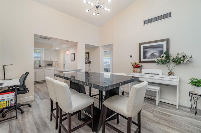 dining area with light hardwood / wood-style flooring, a high ceiling, and a notable chandelier