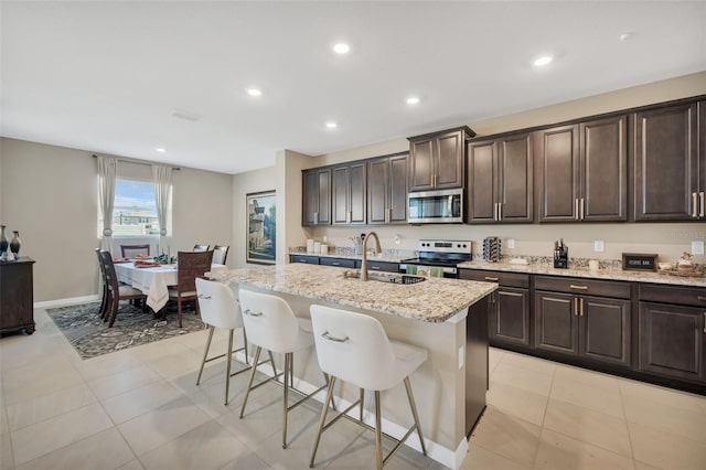 kitchen with appliances with stainless steel finishes, light stone countertops, a kitchen bar, a center island with sink, and sink