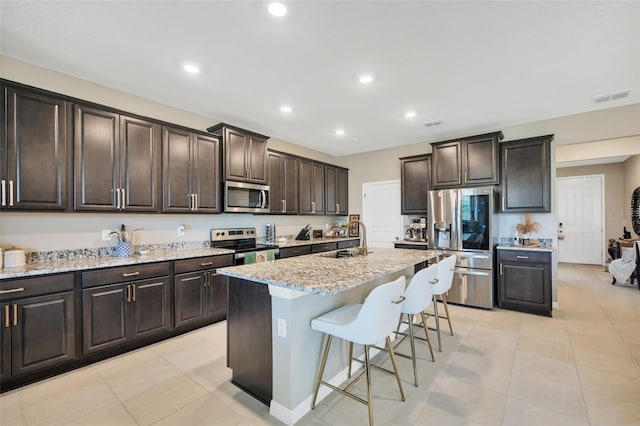 kitchen with an island with sink, sink, dark brown cabinets, appliances with stainless steel finishes, and a kitchen breakfast bar