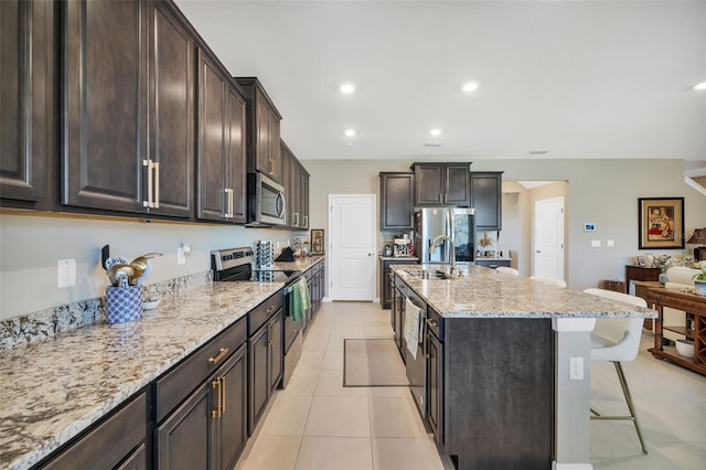 kitchen featuring a breakfast bar area, an island with sink, sink, stainless steel appliances, and light tile patterned floors