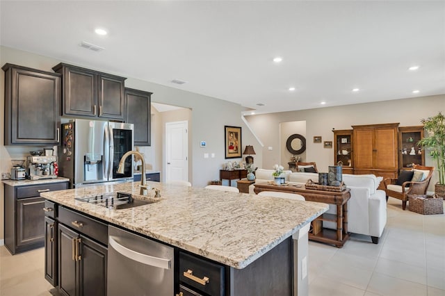 kitchen with light tile patterned flooring, sink, an island with sink, stainless steel appliances, and light stone countertops