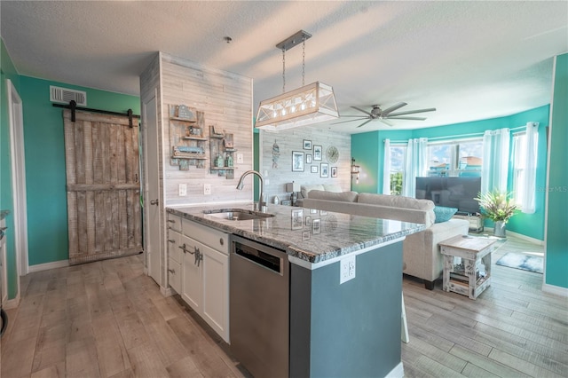 kitchen with ceiling fan, stainless steel dishwasher, decorative light fixtures, white cabinetry, and a barn door