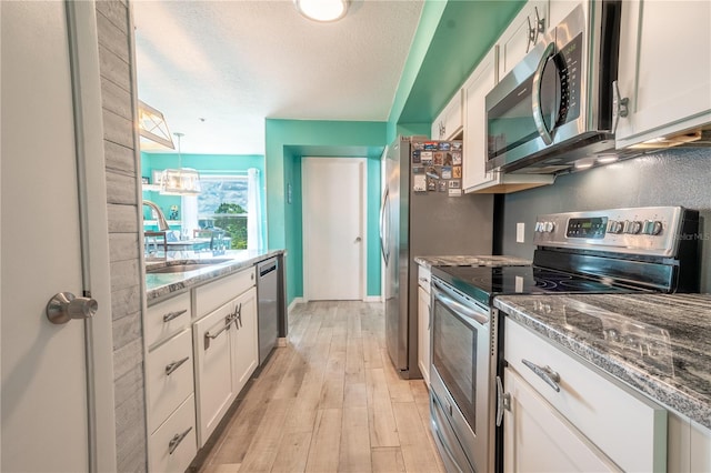 kitchen featuring white cabinets, a textured ceiling, light hardwood / wood-style flooring, stone counters, and appliances with stainless steel finishes