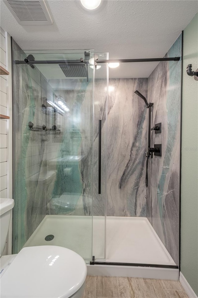 bathroom with a textured ceiling, hardwood / wood-style floors, toilet, and a shower with shower door