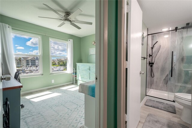 bathroom with tiled shower, vanity, toilet, and ceiling fan