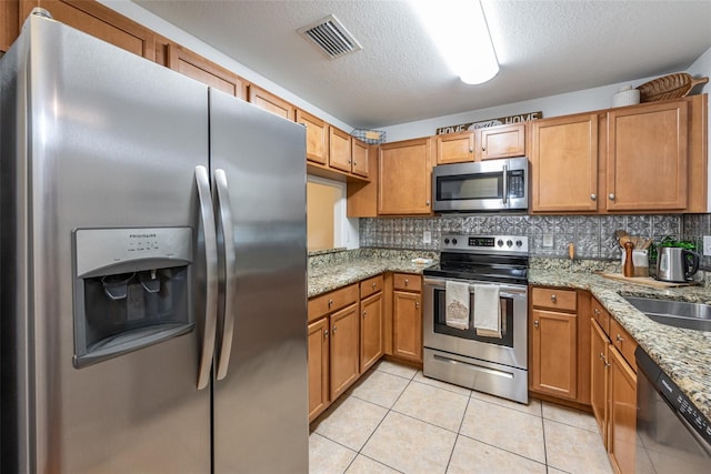 kitchen featuring appliances with stainless steel finishes, light stone countertops, light tile patterned floors, and tasteful backsplash