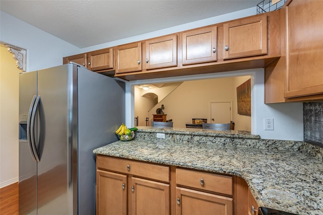 kitchen featuring hardwood / wood-style flooring, light stone countertops, stainless steel fridge, and a textured ceiling