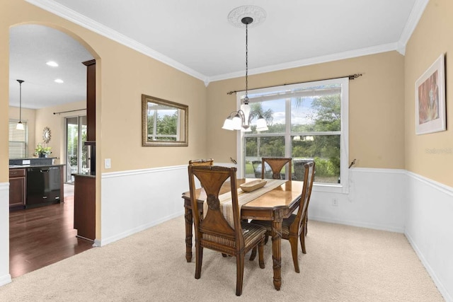 carpeted dining area with an inviting chandelier and ornamental molding