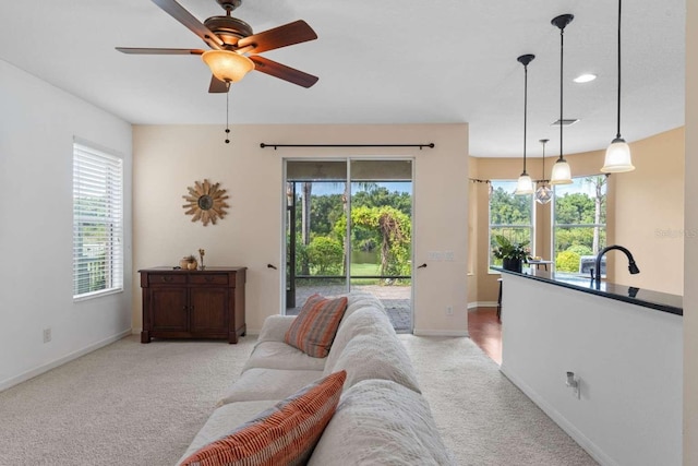 living room with ceiling fan with notable chandelier, light colored carpet, and sink