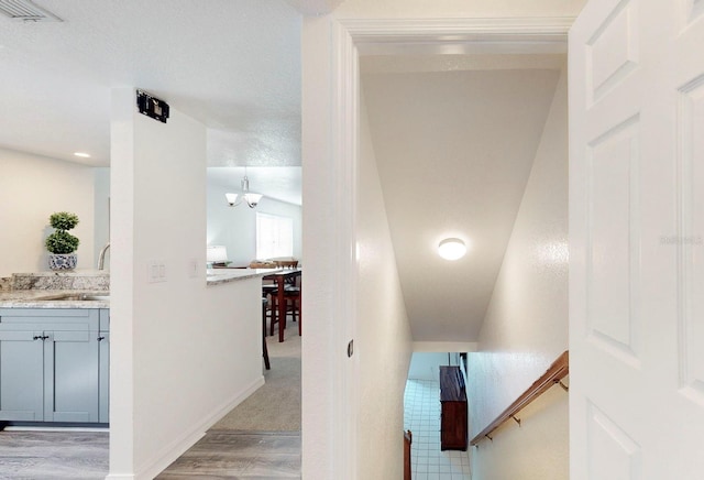 stairway featuring vaulted ceiling, a textured ceiling, hardwood / wood-style floors, sink, and a notable chandelier