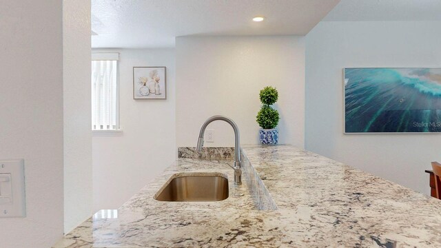 kitchen with kitchen peninsula, light stone counters, a textured ceiling, and sink