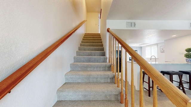 staircase featuring carpet floors, a textured ceiling, and sink