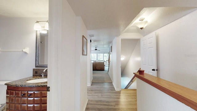 corridor with a textured ceiling, sink, and light hardwood / wood-style flooring