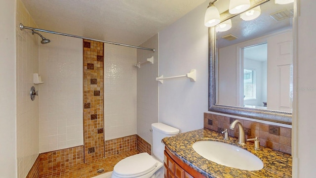 bathroom featuring a textured ceiling, decorative backsplash, tiled shower, vanity, and toilet