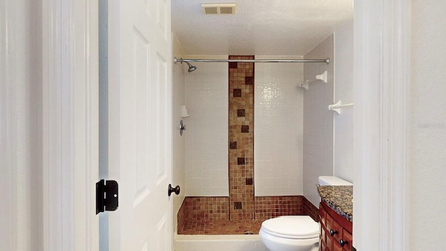 bathroom featuring a textured ceiling, a tile shower, vanity, and toilet