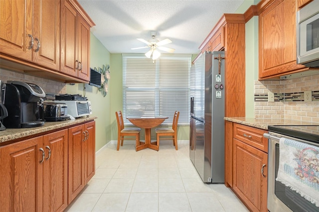 kitchen featuring appliances with stainless steel finishes, light stone counters, tasteful backsplash, light tile patterned floors, and ceiling fan