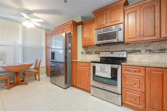 kitchen featuring light stone counters, a textured ceiling, tasteful backsplash, appliances with stainless steel finishes, and ceiling fan