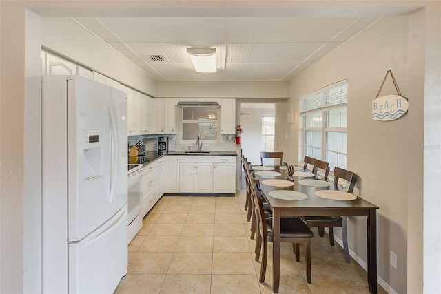 kitchen with decorative backsplash, light tile patterned floors, white appliances, and white cabinetry