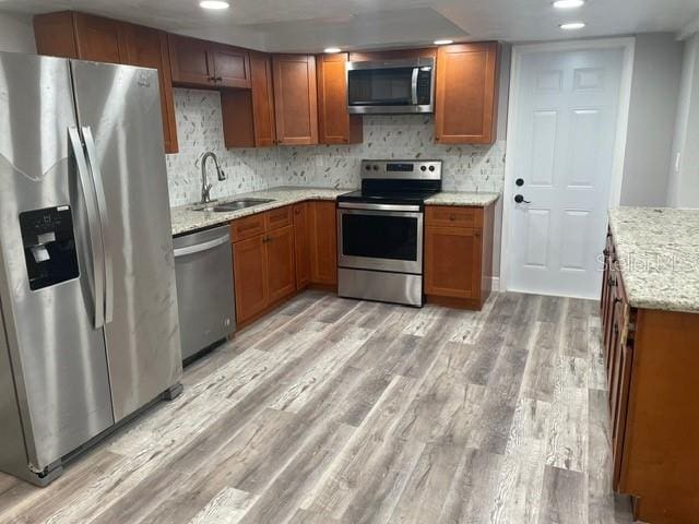 kitchen featuring backsplash, light stone countertops, light wood-type flooring, sink, and stainless steel appliances