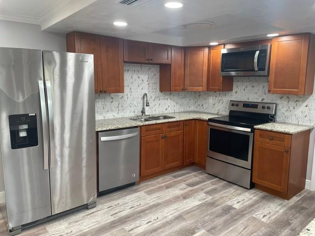 kitchen featuring light stone countertops, sink, stainless steel appliances, crown molding, and light hardwood / wood-style flooring