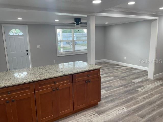 kitchen with light stone countertops, ornamental molding, light hardwood / wood-style flooring, and ceiling fan