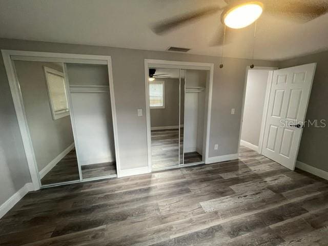 unfurnished bedroom with dark wood-type flooring, two closets, and ceiling fan