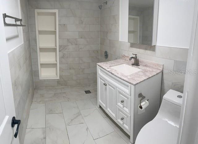 bathroom featuring vanity, toilet, a shower, and tile walls