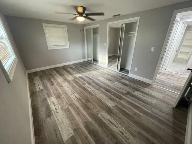 unfurnished bedroom featuring multiple closets, dark wood-type flooring, and ceiling fan