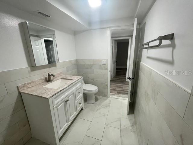 bathroom with toilet, vanity, and tile walls